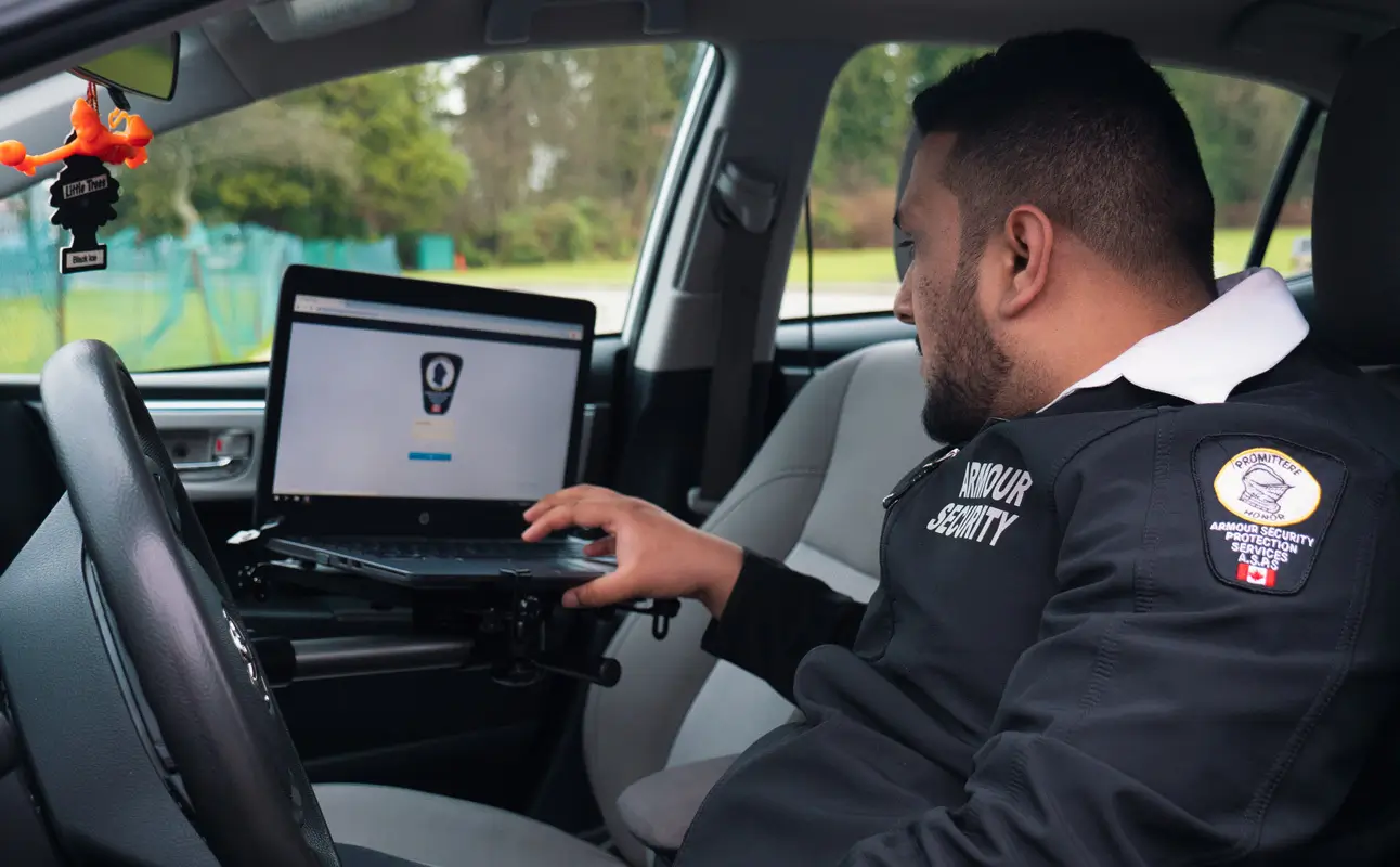 An Armour Security guard completing a report on a laptop mounted inside a patrol vehicle
