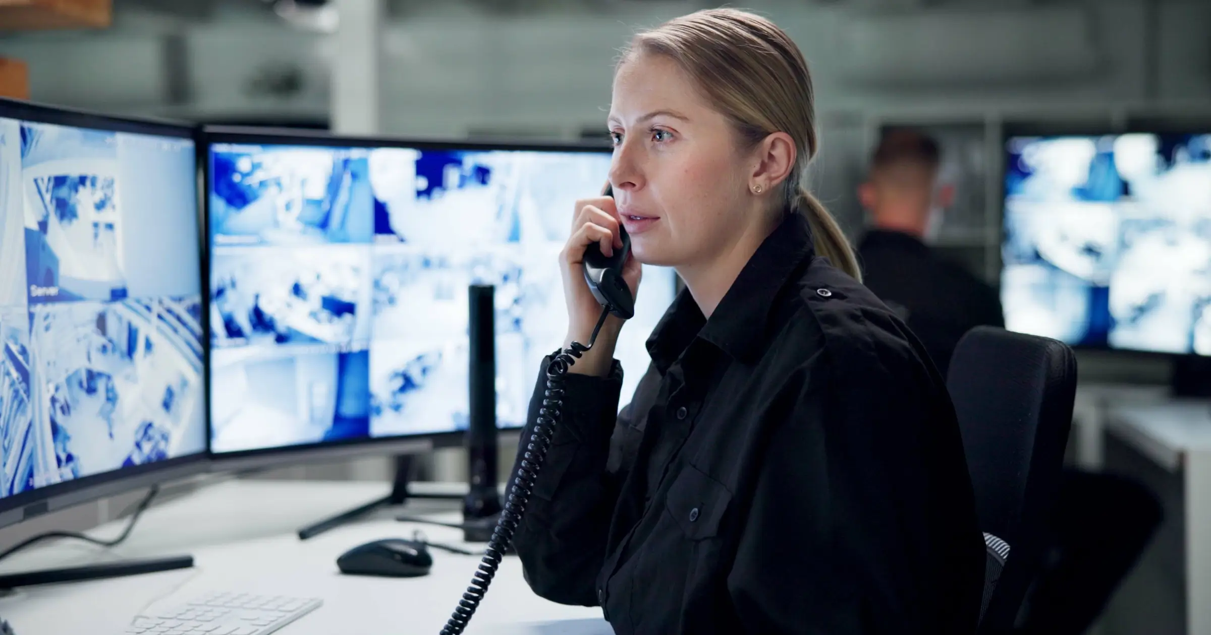 Security supervisor on a desk phone at a control room desk with CCTV monitors